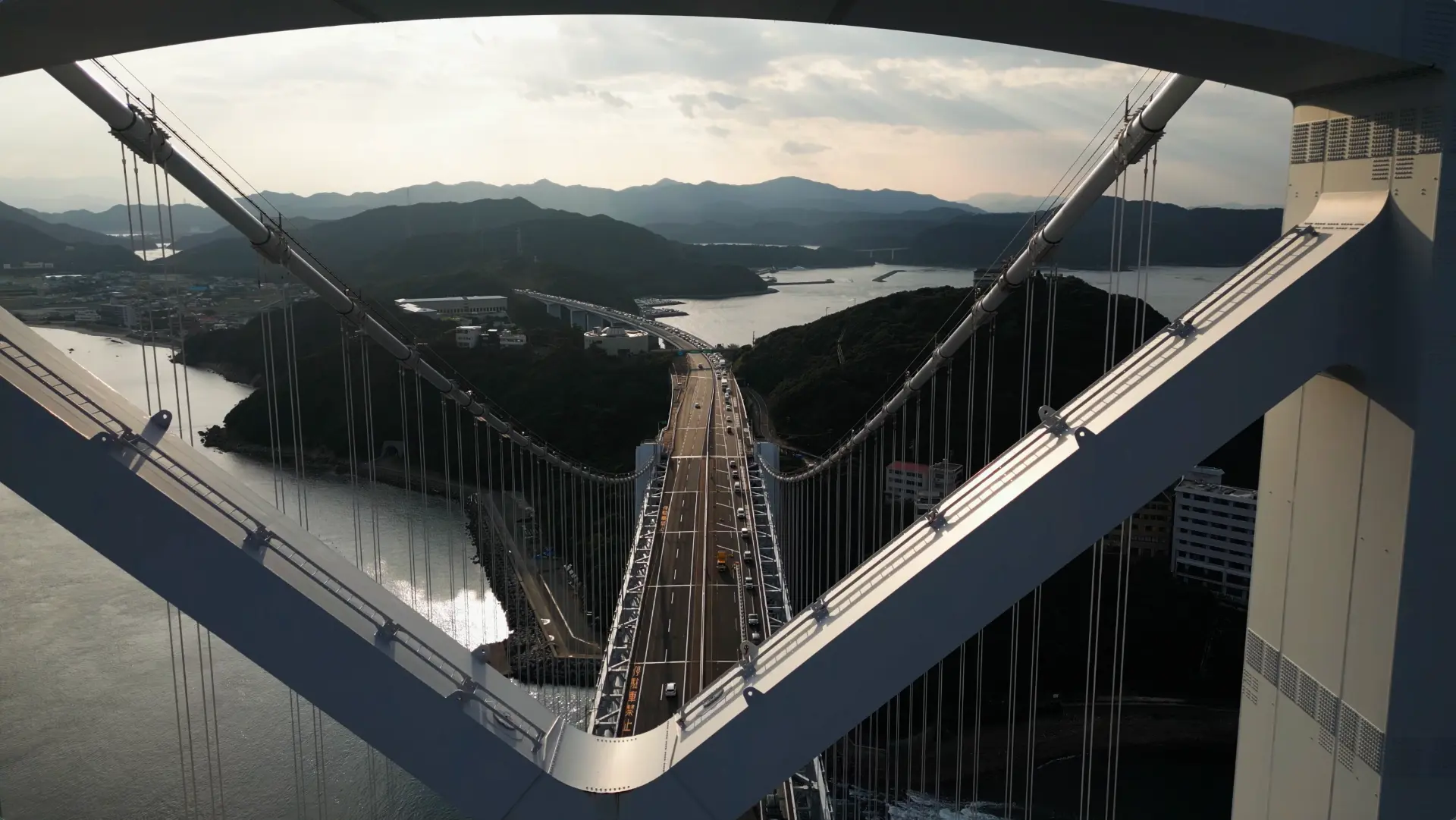 Looking down the length of a suspension bridge towards a hazy bay